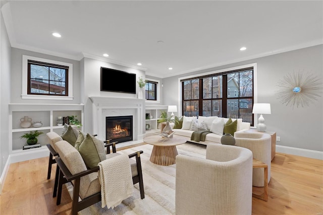 living room with a high end fireplace, light wood-style flooring, baseboards, and ornamental molding