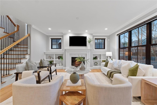 living area featuring stairway, light wood-style flooring, recessed lighting, a high end fireplace, and crown molding