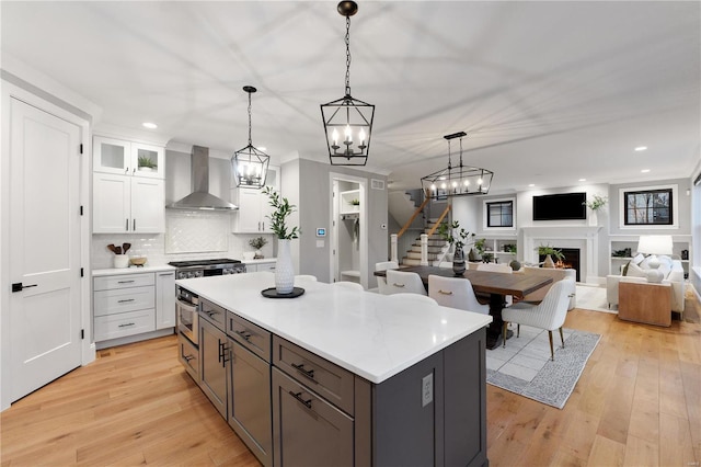 kitchen with a kitchen island, wall chimney range hood, light countertops, a lit fireplace, and white cabinetry