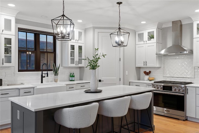 kitchen with gas stove, a sink, light countertops, wall chimney exhaust hood, and a center island