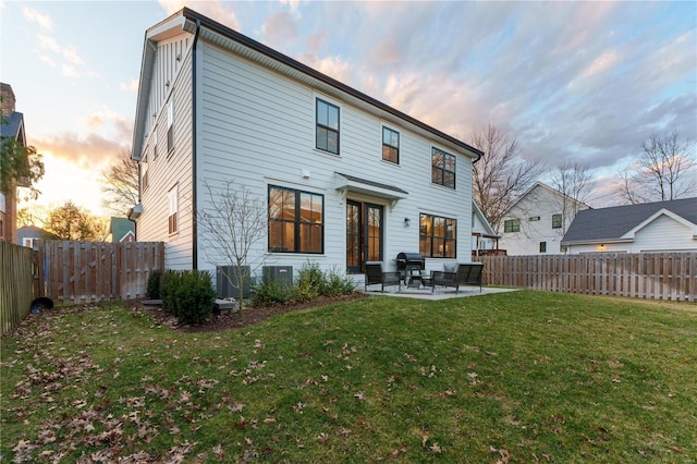 back of house at dusk with a fenced backyard, a yard, and a patio