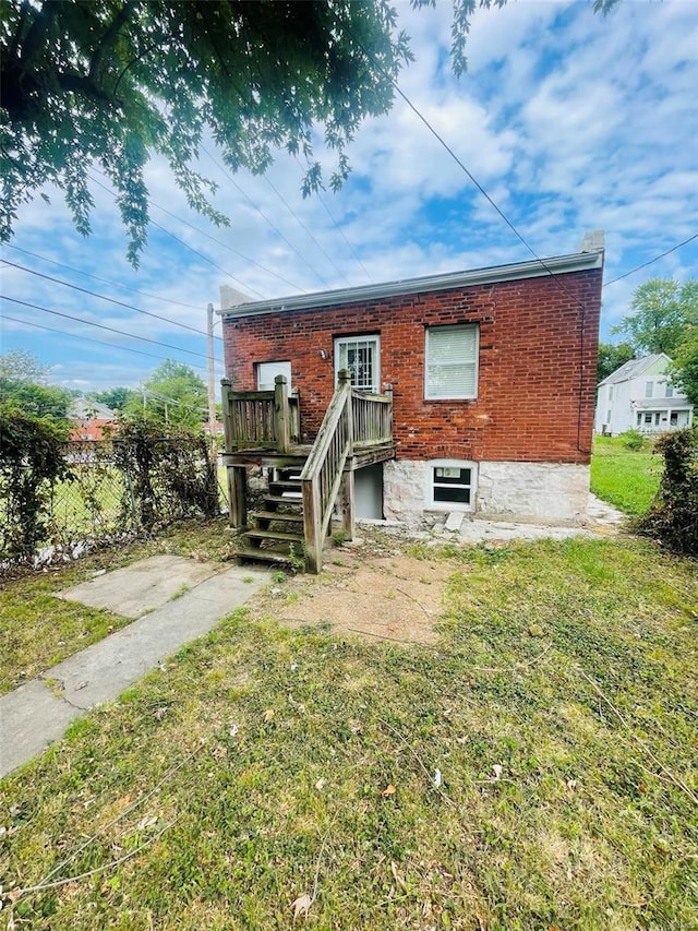 rear view of house featuring brick siding, a lawn, and fence