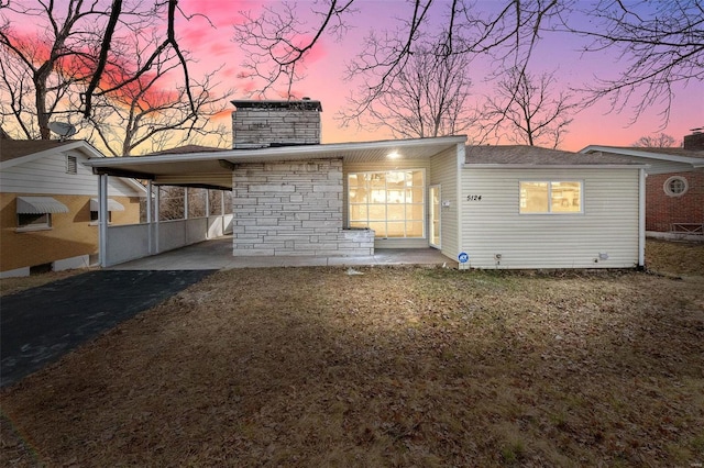 view of front of home featuring driveway, a carport, and a chimney