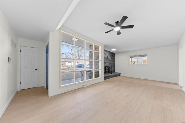 unfurnished living room featuring visible vents, light wood-style flooring, a stone fireplace, baseboards, and ceiling fan