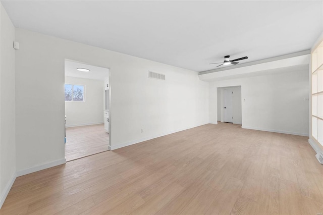 empty room featuring a ceiling fan, visible vents, light wood finished floors, and baseboards