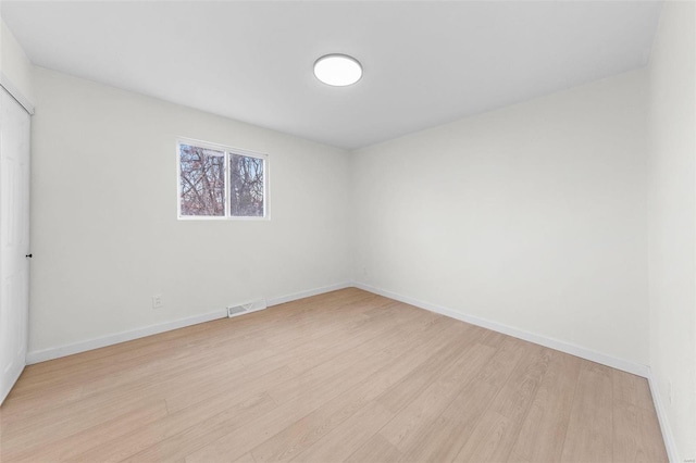 empty room with light wood-style floors, visible vents, and baseboards