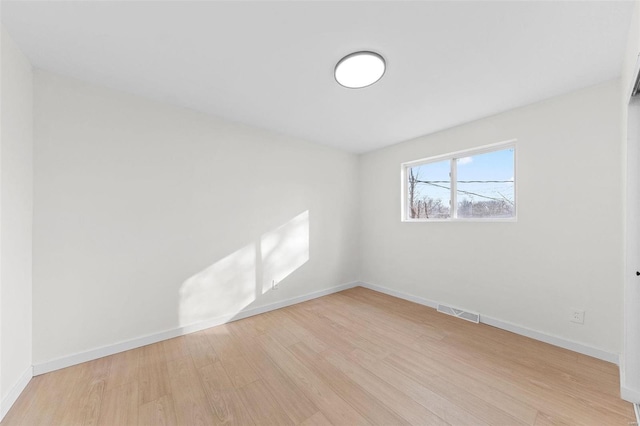 spare room with wood finished floors, visible vents, and baseboards