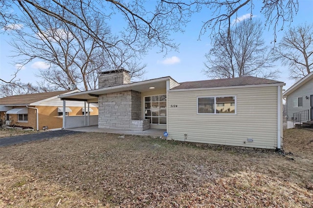 back of property featuring a carport, aphalt driveway, and a chimney