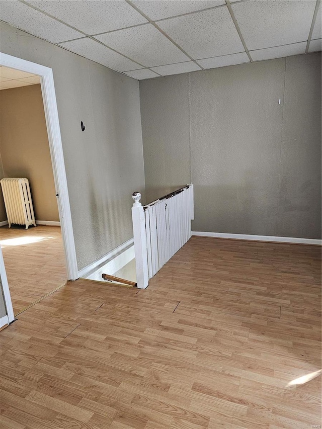 spare room featuring a drop ceiling, baseboards, wood finished floors, and radiator heating unit