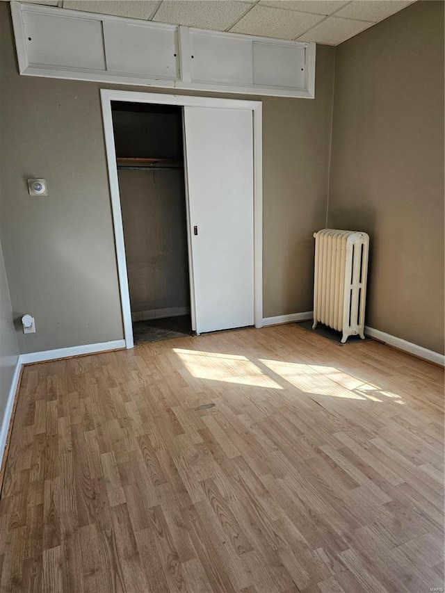 unfurnished bedroom with radiator, a paneled ceiling, baseboards, and wood finished floors