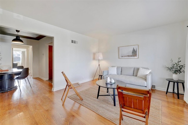 living room with light wood finished floors, visible vents, and baseboards