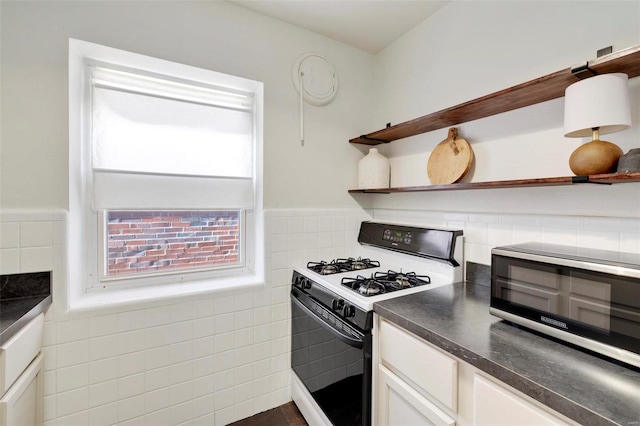 kitchen featuring open shelves, gas range gas stove, dark countertops, and tile walls