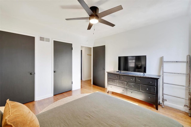 bedroom featuring visible vents, multiple closets, wood finished floors, baseboards, and ceiling fan