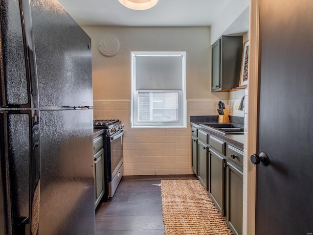 kitchen featuring stainless steel gas range oven, dark countertops, freestanding refrigerator, tile walls, and a sink