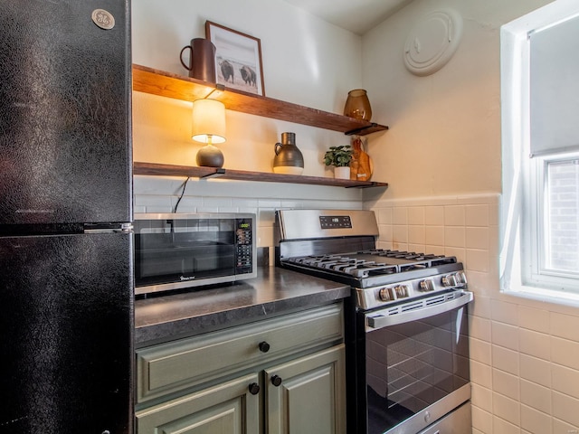 kitchen featuring dark countertops, a toaster, stainless steel range with gas stovetop, freestanding refrigerator, and tile walls