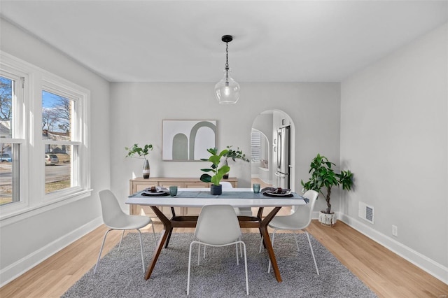 dining area with light wood finished floors, visible vents, arched walkways, and baseboards