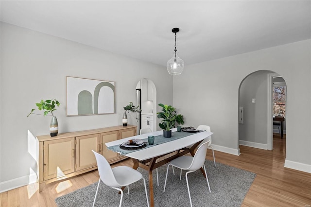 dining space with light wood-type flooring, arched walkways, and baseboards