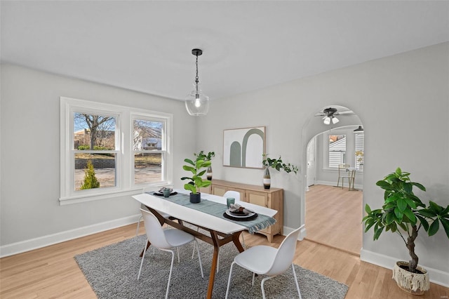 dining space featuring baseboards, arched walkways, and light wood finished floors