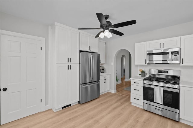 kitchen featuring stainless steel appliances, arched walkways, light wood-style flooring, and light countertops