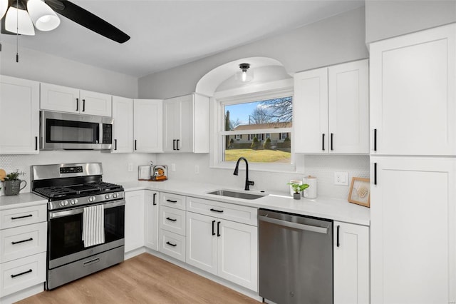 kitchen with a sink, stainless steel appliances, light countertops, light wood-style floors, and white cabinetry