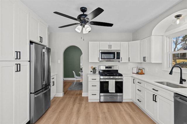 kitchen with a sink, arched walkways, appliances with stainless steel finishes, and white cabinets