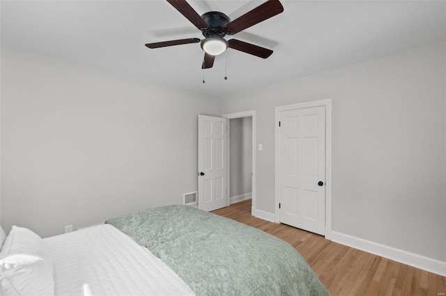 bedroom with a ceiling fan, wood finished floors, visible vents, and baseboards