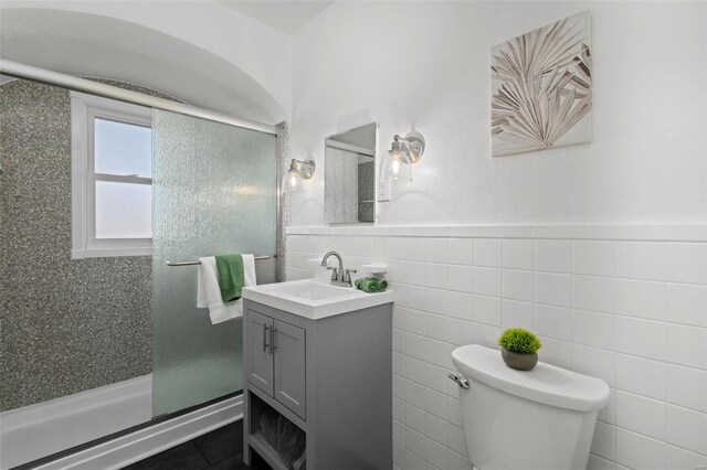 full bathroom with vanity, tile walls, toilet, and a stall shower