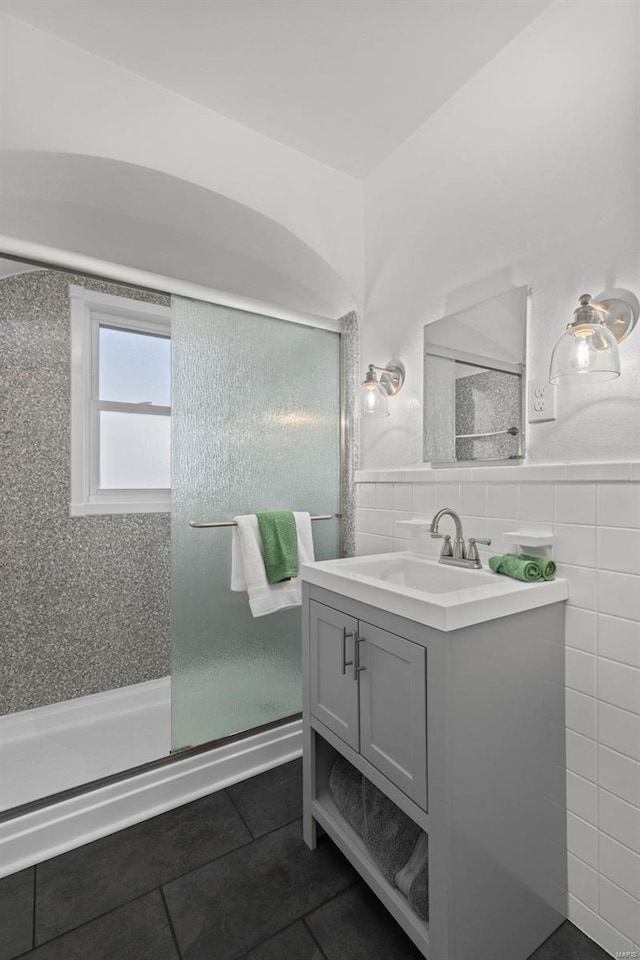 full bathroom with tile patterned floors, tile walls, wainscoting, a shower stall, and vanity