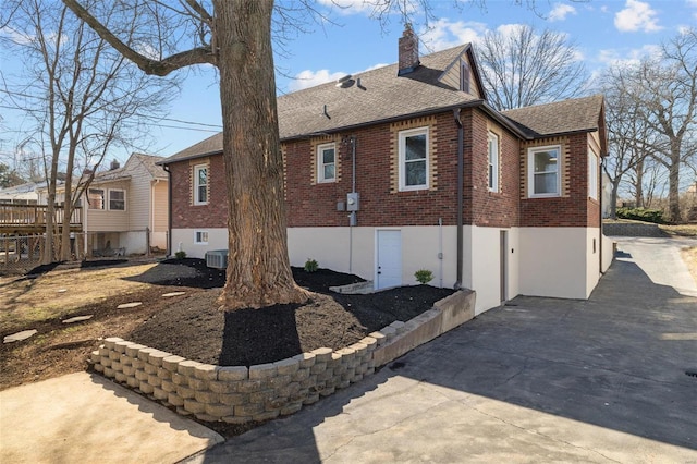 view of side of property with brick siding, central air condition unit, a chimney, and roof with shingles