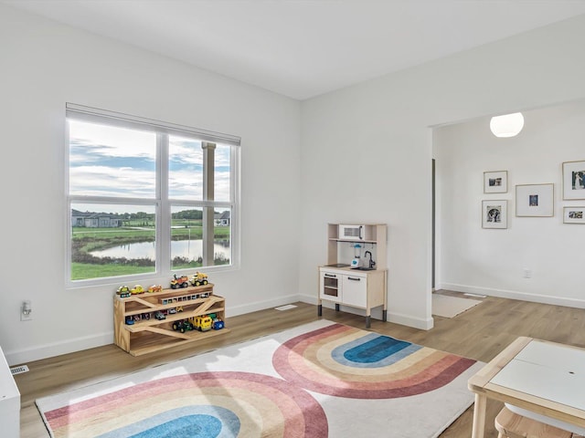 rec room featuring visible vents, light wood-style flooring, baseboards, and a water view