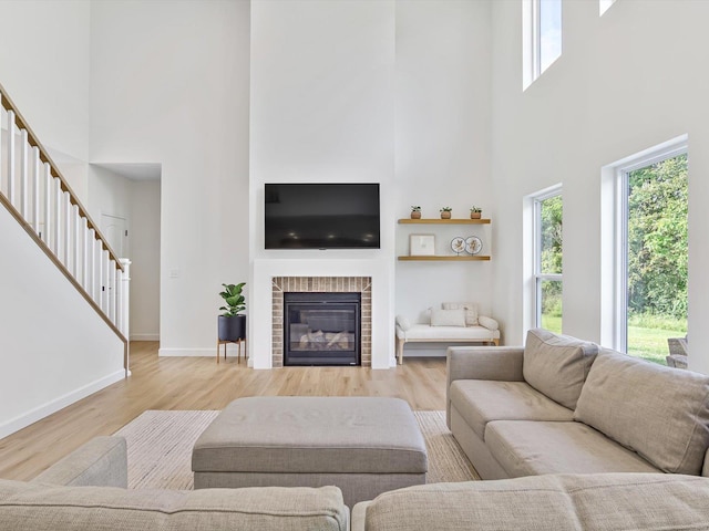 living area with stairway, wood finished floors, baseboards, a high ceiling, and a glass covered fireplace