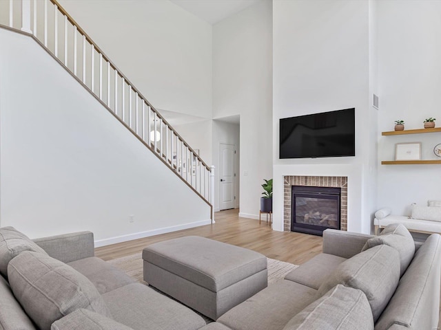 living room featuring light wood-type flooring, baseboards, a glass covered fireplace, and stairway