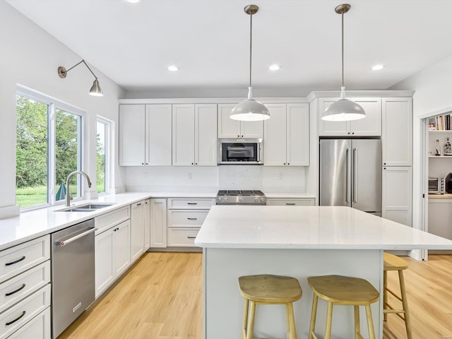 kitchen featuring a kitchen island, a breakfast bar area, appliances with stainless steel finishes, light wood-style floors, and a sink