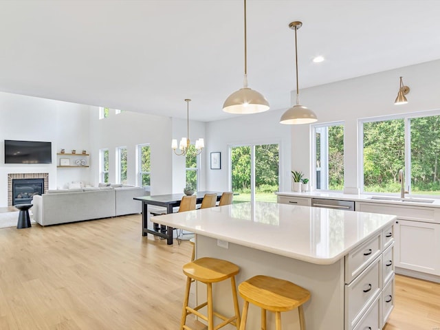 kitchen featuring a kitchen island, dishwasher, light wood-style flooring, white cabinets, and a sink