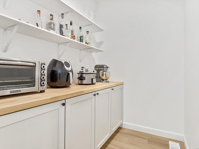 bar featuring a toaster, visible vents, baseboards, and light wood-style floors