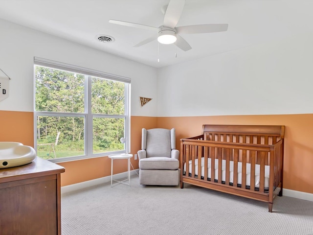 carpeted bedroom with visible vents, ceiling fan, a crib, and baseboards