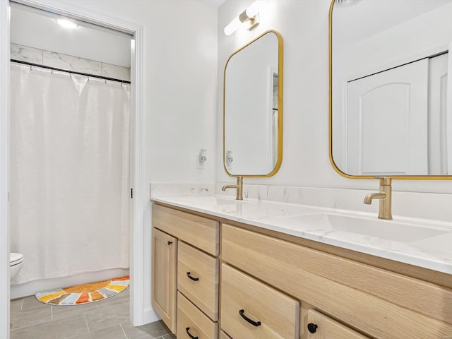 bathroom featuring a shower with shower curtain, double vanity, toilet, and a sink