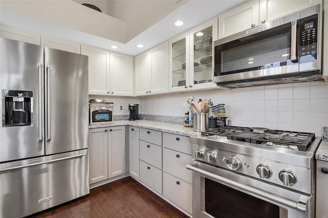 kitchen with backsplash, dark wood finished floors, appliances with stainless steel finishes, glass insert cabinets, and light stone countertops