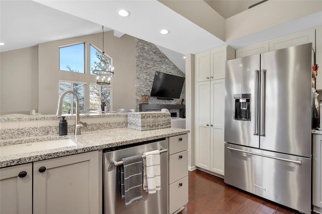 kitchen with light stone counters, dark wood-style flooring, a sink, stainless steel appliances, and decorative light fixtures