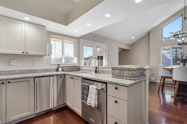 kitchen with lofted ceiling, a peninsula, dark wood-style floors, fridge, and a sink