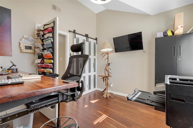 office featuring wood finished floors, visible vents, baseboards, vaulted ceiling, and a barn door