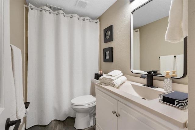 full bathroom with visible vents, toilet, vanity, and a textured wall