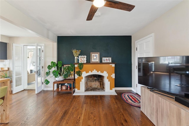 living area featuring baseboards, a fireplace with flush hearth, wood finished floors, and a ceiling fan