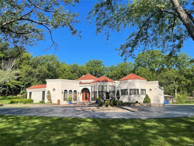 mediterranean / spanish house featuring a tile roof, a front lawn, aphalt driveway, and stucco siding