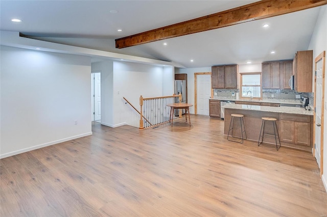 kitchen featuring lofted ceiling with beams, backsplash, light wood-style floors, a peninsula, and baseboards