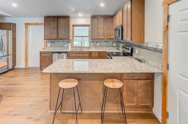 kitchen with light wood-type flooring, a sink, backsplash, appliances with stainless steel finishes, and a peninsula