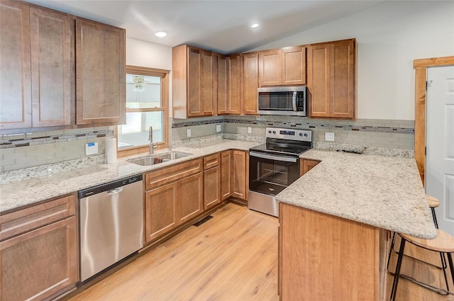 kitchen with a breakfast bar, a peninsula, lofted ceiling, a sink, and appliances with stainless steel finishes