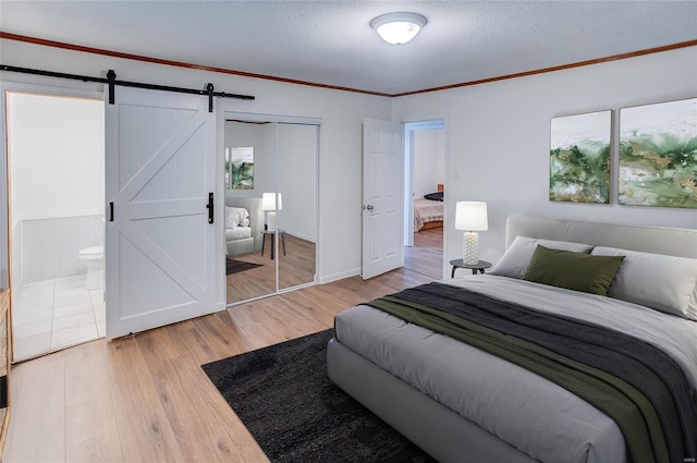 bedroom with a textured ceiling, wood finished floors, a barn door, a closet, and crown molding