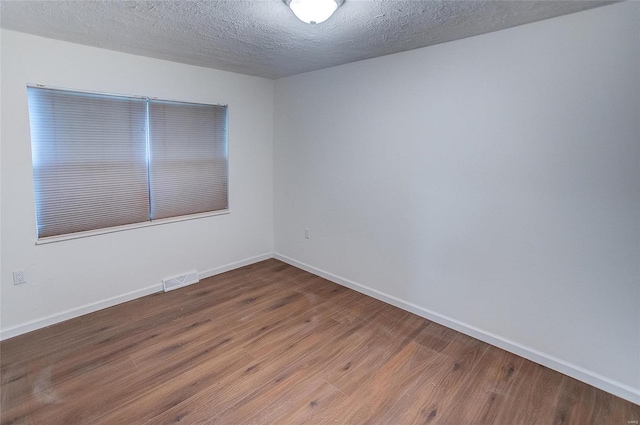 unfurnished room featuring a textured ceiling, wood finished floors, visible vents, and baseboards