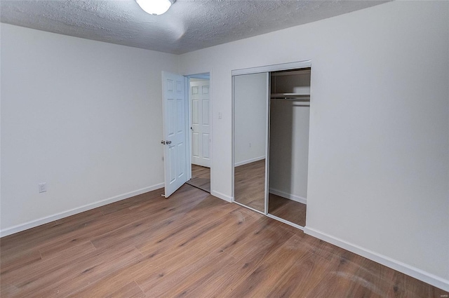 unfurnished bedroom featuring a closet, a textured ceiling, baseboards, and wood finished floors